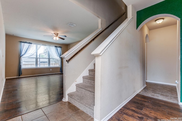 staircase with a ceiling fan, wood finished floors, baseboards, visible vents, and arched walkways