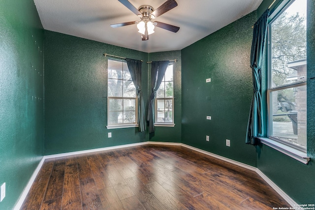 empty room featuring a textured wall, baseboards, ceiling fan, and wood finished floors
