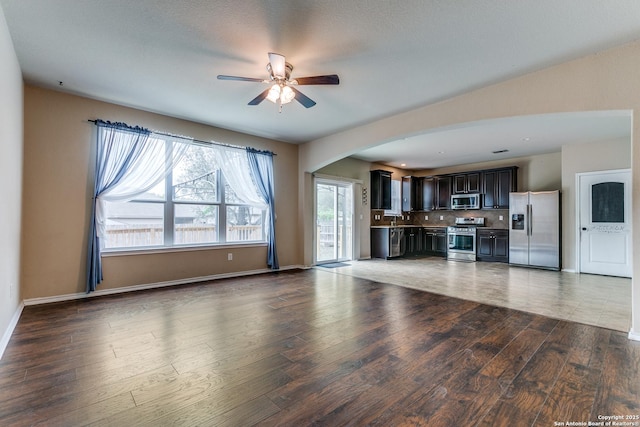 unfurnished living room with arched walkways, baseboards, ceiling fan, and wood finished floors
