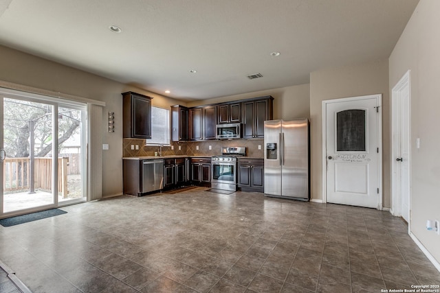 kitchen with baseboards, dark brown cabinets, tasteful backsplash, appliances with stainless steel finishes, and a sink