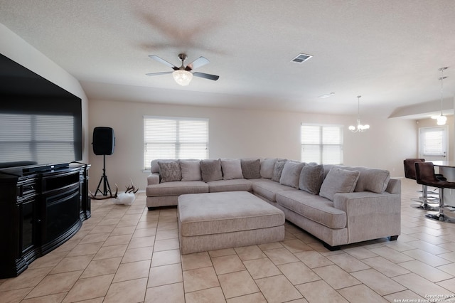 living area featuring light tile patterned flooring, ceiling fan with notable chandelier, visible vents, and a healthy amount of sunlight