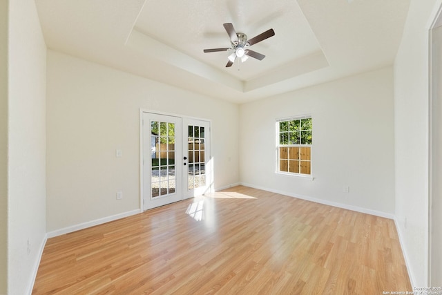 unfurnished room with a tray ceiling, baseboards, light wood-type flooring, and french doors