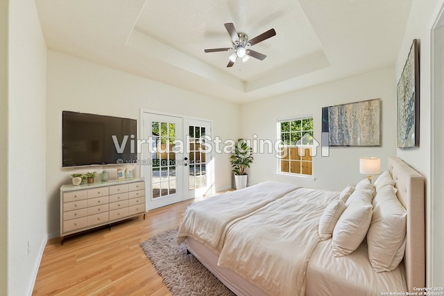 bedroom with french doors, access to outside, a raised ceiling, light wood-style floors, and ceiling fan