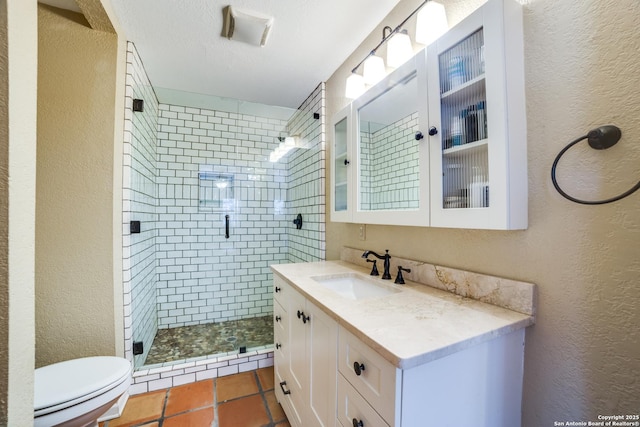 bathroom with toilet, vanity, a textured wall, and a shower stall