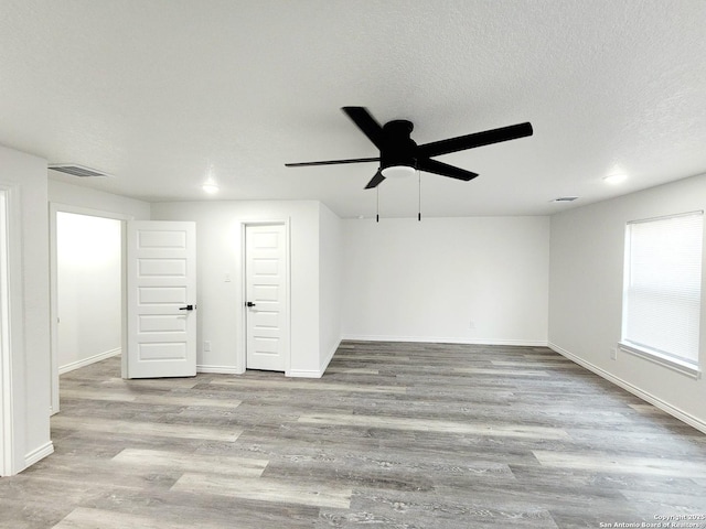 spare room featuring a textured ceiling, visible vents, baseboards, wood finished floors, and a ceiling fan