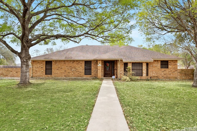 single story home with brick siding, fence, roof with shingles, and a front yard