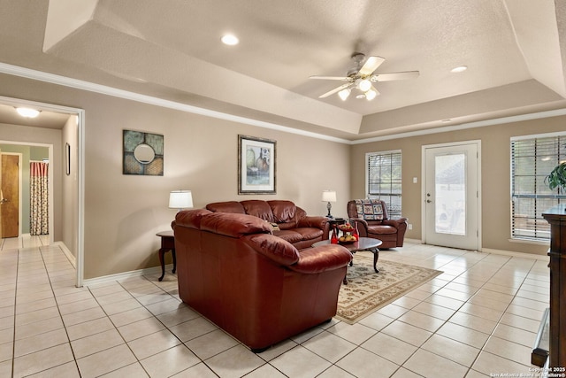 living area with light tile patterned flooring, a textured ceiling, baseboards, ceiling fan, and a raised ceiling