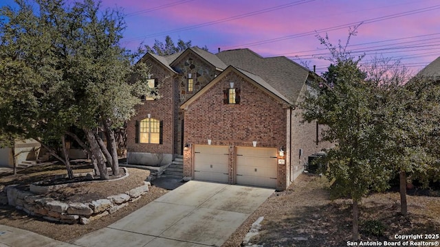 view of front facade with driveway, central air condition unit, brick siding, a shingled roof, and a garage