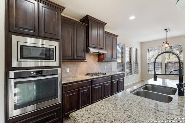 kitchen with stainless steel appliances, under cabinet range hood, backsplash, a sink, and light stone countertops