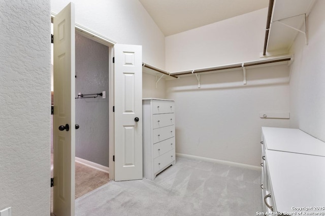 walk in closet with vaulted ceiling and light colored carpet