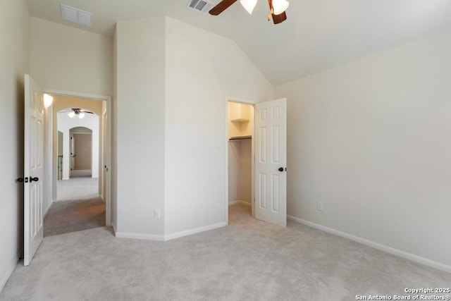 unfurnished bedroom featuring light colored carpet, visible vents, arched walkways, and a walk in closet