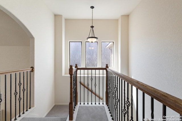 corridor with arched walkways, an upstairs landing, and carpet flooring