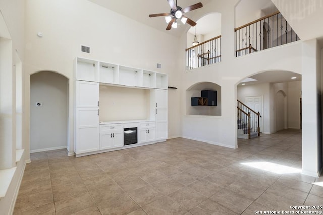unfurnished living room with visible vents, baseboards, ceiling fan, stairway, and arched walkways