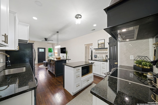 kitchen featuring a sink, black microwave, a center island, ceiling fan, and dark wood-type flooring