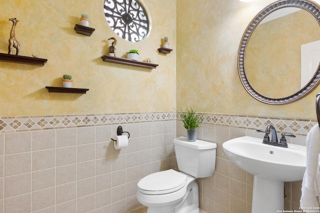 bathroom featuring toilet, a wainscoted wall, a sink, and tile walls