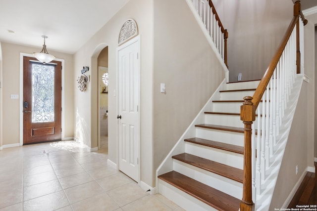 foyer featuring arched walkways, baseboards, stairway, and light tile patterned floors