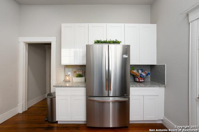 144 Ward Ave, San Antonio, TX 78223 - kitchen with freestanding refrigerator, white cabinets, light stone countertops, and tasteful backsplash