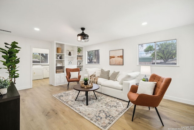 living room featuring light wood-style flooring, visible vents, washer and dryer, and a wealth of natural light