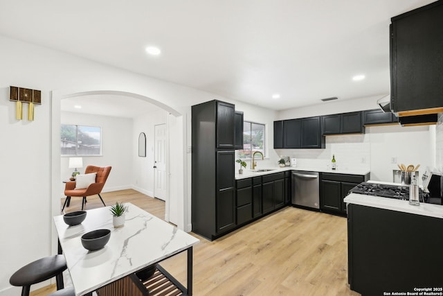 kitchen featuring light countertops, a sink, stainless steel dishwasher, arched walkways, and dark cabinets