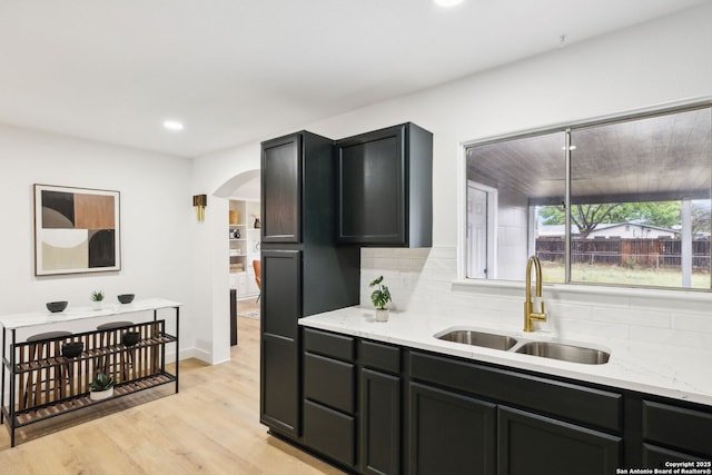 kitchen featuring a sink, tasteful backsplash, light wood-type flooring, arched walkways, and recessed lighting