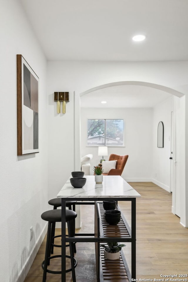 dining area featuring arched walkways, baseboards, light wood-style flooring, and recessed lighting