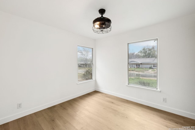 spare room featuring light wood finished floors, baseboards, and a healthy amount of sunlight