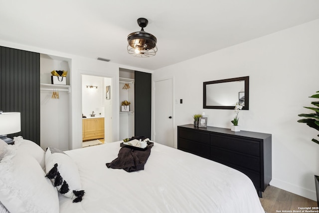 bedroom featuring baseboards, visible vents, wood finished floors, and ensuite bathroom