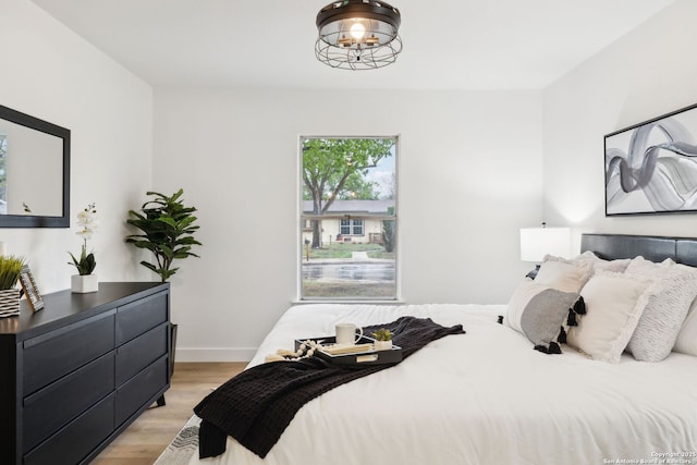 bedroom with baseboards, an inviting chandelier, and light wood finished floors
