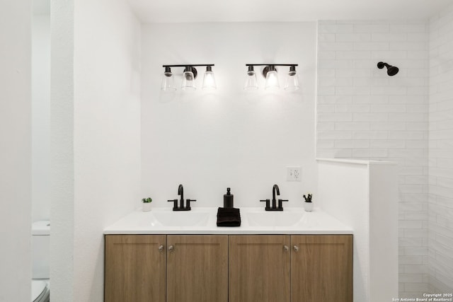 bathroom with toilet, a sink, double vanity, and a tile shower