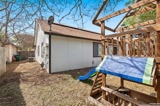 rear view of property featuring roof with shingles, central AC, fence, and roof mounted solar panels