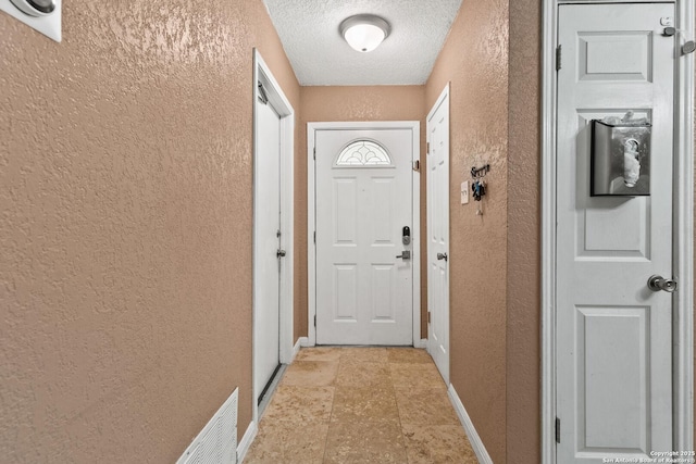 doorway to outside with a textured wall, a textured ceiling, baseboards, and visible vents