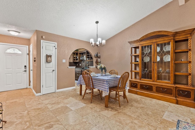 dining room featuring a notable chandelier, a textured ceiling, baseboards, arched walkways, and a textured wall