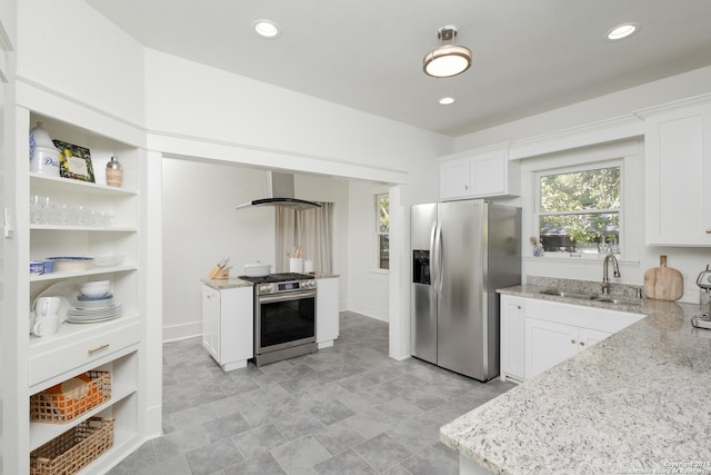 kitchen featuring light stone countertops, appliances with stainless steel finishes, white cabinetry, a sink, and wall chimney range hood