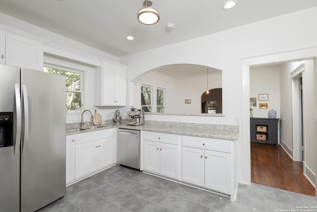 kitchen with a sink, light stone countertops, appliances with stainless steel finishes, white cabinets, and arched walkways