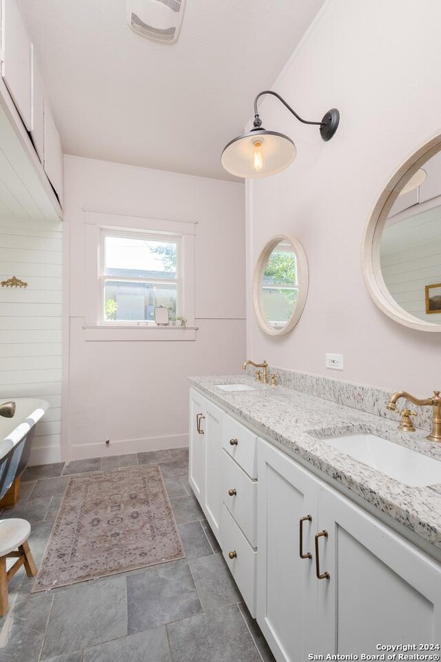full bath with stone finish floor, double vanity, visible vents, and a sink