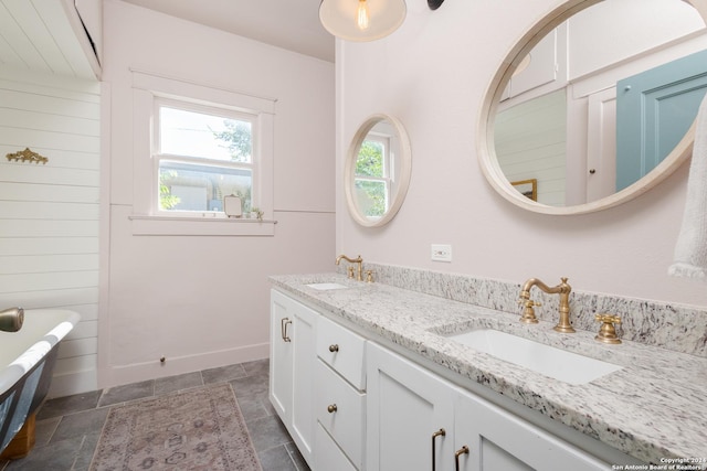 bathroom featuring a freestanding tub, stone finish floor, baseboards, a sink, and double vanity