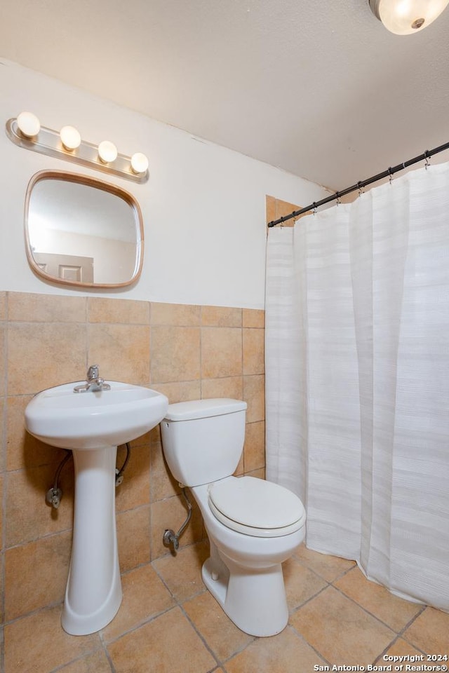 full bathroom featuring toilet, tile patterned floors, tile walls, and wainscoting