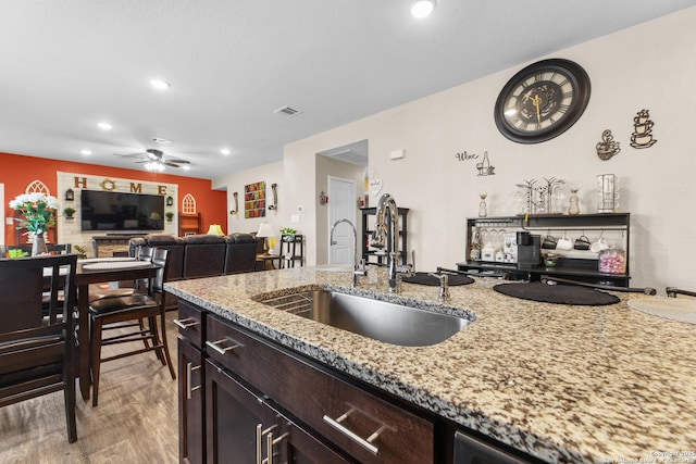 kitchen with a sink, light stone counters, visible vents, ceiling fan, and wood finished floors
