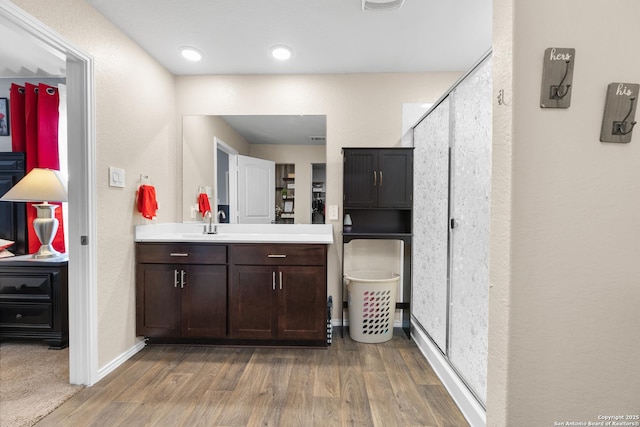 bathroom featuring baseboards, wood finished floors, a stall shower, and vanity