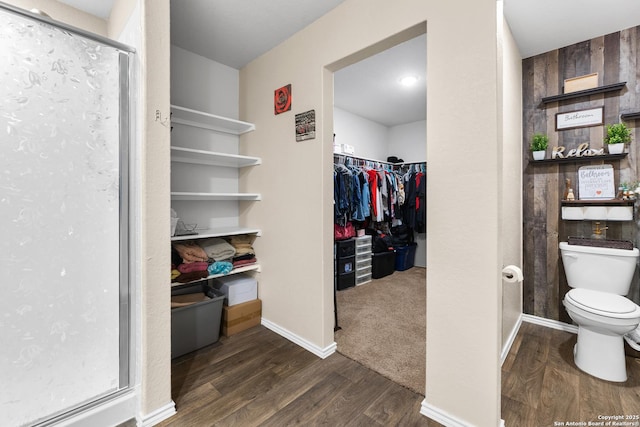 bathroom with toilet, wood finished floors, a walk in closet, a shower with shower door, and baseboards