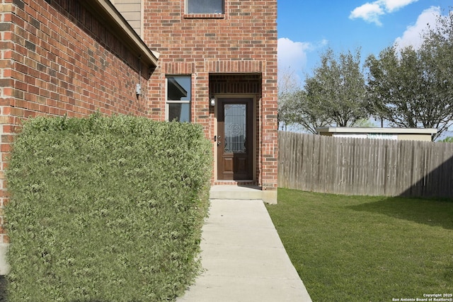 entrance to property featuring brick siding, fence, and a yard