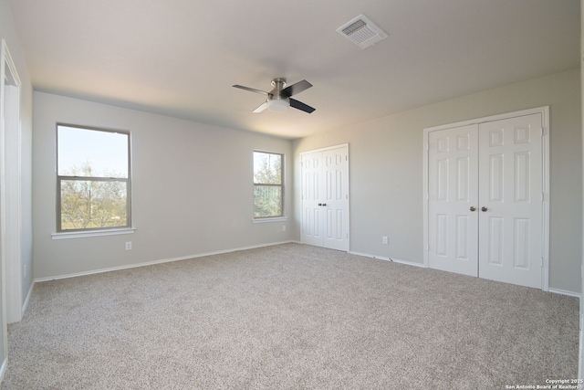 unfurnished bedroom featuring two closets, carpet flooring, baseboards, visible vents, and a ceiling fan