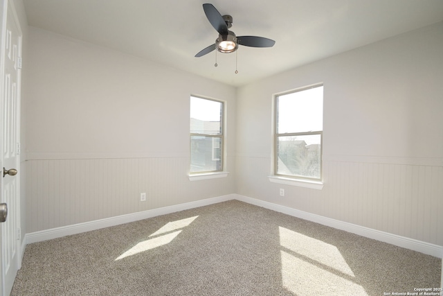 spare room featuring wainscoting, carpet, and a ceiling fan