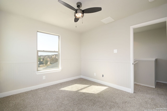 empty room with carpet flooring, a wainscoted wall, and ceiling fan