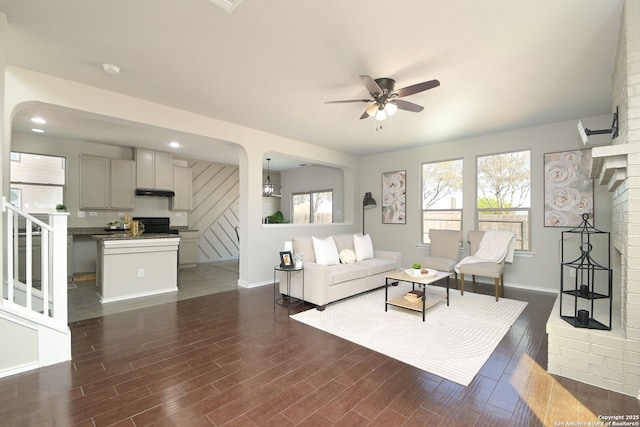 living room featuring baseboards, dark wood-style flooring, ceiling fan, and stairway