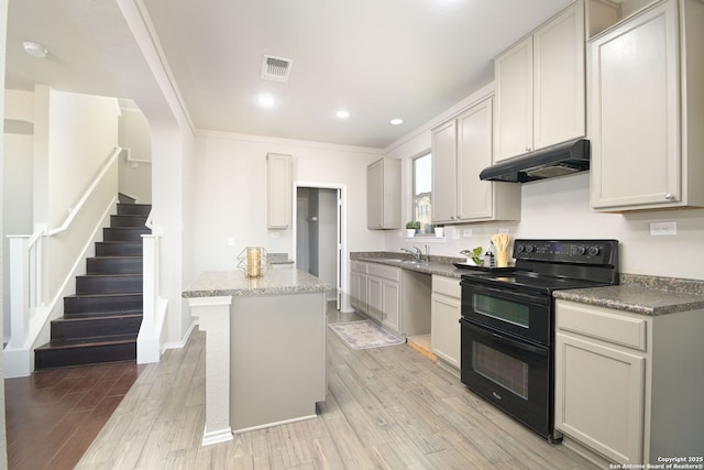 kitchen featuring light wood-style flooring, visible vents, under cabinet range hood, range with two ovens, and a center island