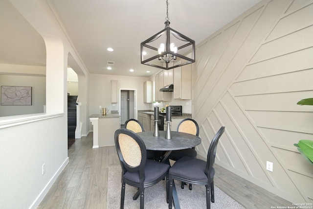 dining area featuring a notable chandelier, light wood-type flooring, a decorative wall, ornamental molding, and recessed lighting
