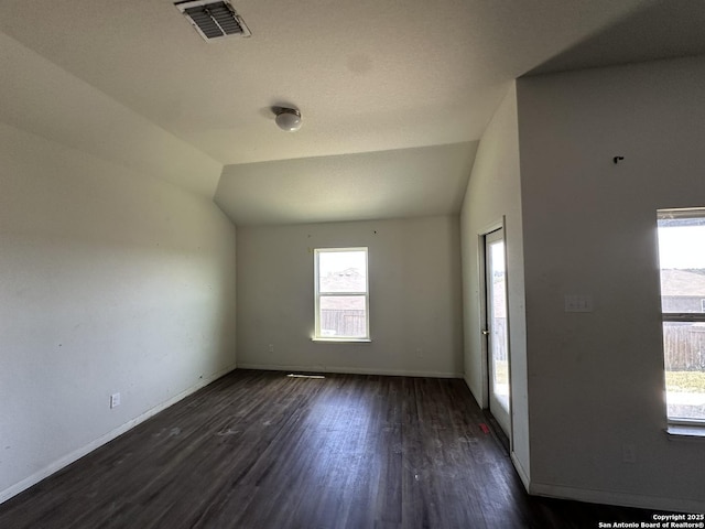 unfurnished room featuring baseboards, visible vents, dark wood-style flooring, and vaulted ceiling