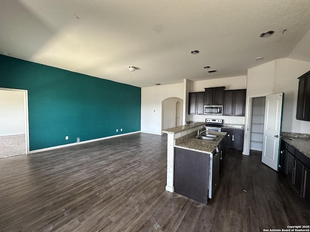 kitchen featuring a kitchen island with sink, stainless steel appliances, dark wood finished floors, arched walkways, and open floor plan