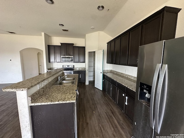kitchen with arched walkways, a sink, dark wood-type flooring, and appliances with stainless steel finishes